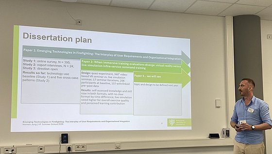 Vortragender rechts vor seiner Präsentation. Die aktuelle Slide ist mit "Dissertation Plan" betietelt.